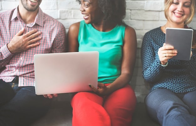A diverse group of people sitting together, laughing and pointing at a laptop screen, suggesting a shared viewing experience of a popular series.