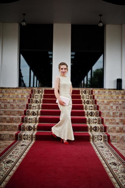 A famous K-drama actress, elegantly dressed in a designer gown, poses on the red carpet at a Hollywood awards ceremony, surrounded by flashing cameras and international media.