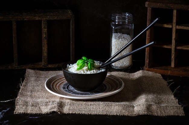 A rustic Korean dining table setup with several small banchan dishes, a bowl of rice, and a pair of long metal chopsticks, ready for a meal.