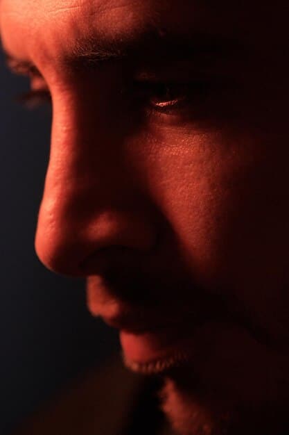 A close-up, shadowed shot of a character's face contorted in fear, illuminated only by a flickering light source from behind, emphasizing paranoia and dread.