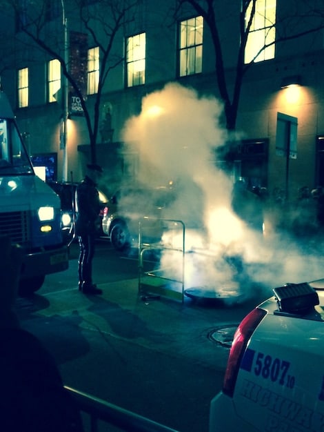 A cinematic still from a suspenseful scene in a crime series. Police cars surround a building, and a group of detectives are conferring. The lighting is dramatic, and the atmosphere is tense. Elements like these solidify the thematic setting of the show.